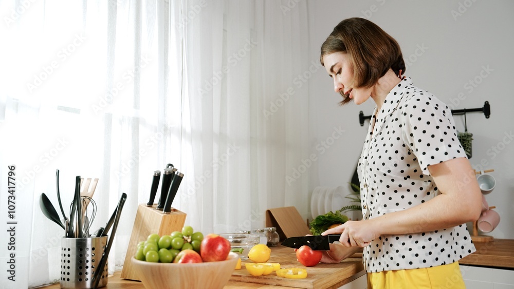Energetic mother making salad for breakfast at modern kitchen while chopping vegetable surrounded with kitchenware. Smart female house keeper cooking and preparing food. Healthy lifestyle. Pedagogy. Energetic mother making salad for breakfast at modern kitchen while chopping vegetable surrounded with kitchenware. Smart female house keeper cooking and preparing food. Healthy lifestyle. Pedagogy.