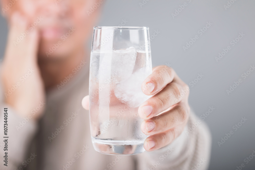 Man holding a glass of cold water with ice, showing a slight grimace due to tooth sensitivity. Image reflects the discomfort of consuming cold foods or drinks, highlighting dental health concerns Man holding a glass of cold water with ice, showing a slight grimace due to tooth sensitivity. Image reflects the discomfort of consuming cold foods or drinks, highlighting dental health concerns