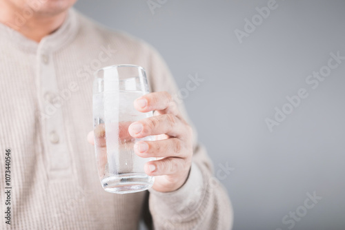 Man holding a glass of cold water with ice, showing a slight grimace due to tooth sensitivity. Image reflects the discomfort of consuming cold foods or drinks, highlighting dental health concerns