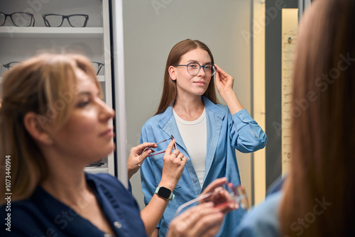 Customer adjusting glasses while optician observes