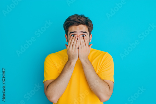 A shy man covered her face with his hands on a blue background. shame people, hiding identity, social anxiety concept. photo