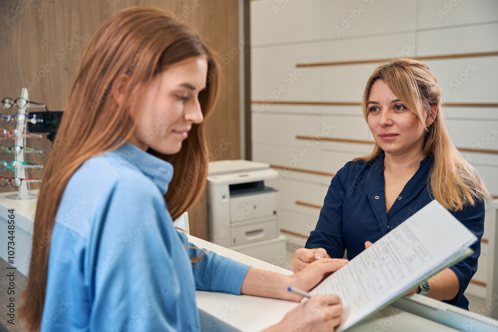 Female adult patient reviewing documents with receptionist Female adult patient reviewing documents with receptionist