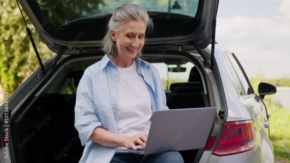 Happy smiling Caucasian elderly business woman female businesswoman aged tourist freelancer working laptop online work computer connection wifi sitting on opened automobile car trunk outdoors nature Happy smiling Caucasian elderly business woman female businesswoman aged tourist freelancer working laptop online work computer connection wifi sitting on opened automobile car trunk outdoors nature