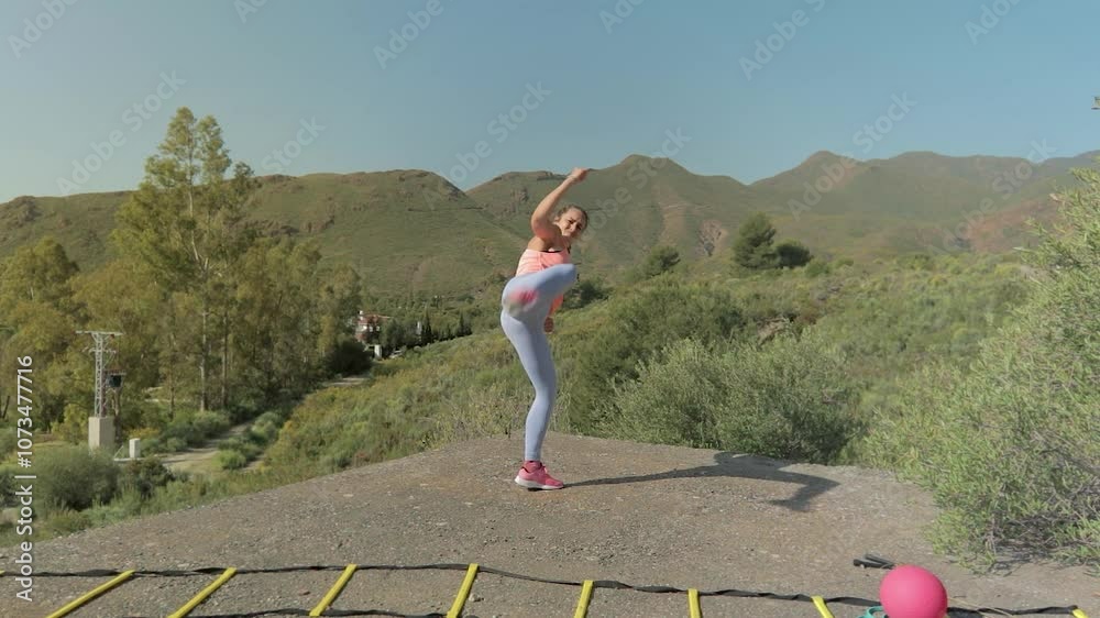 Beautiful Woman Shadowboxing with kick in the Green Nature with Mountains in the Background. Hermosa Mujer Haciendo boxeo al aire en la Naturaleza Verde con Montañas de Fondo
