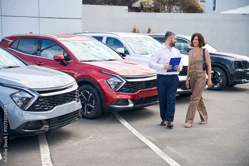 Female client talking with salesman manager at car salon showroom outdoors