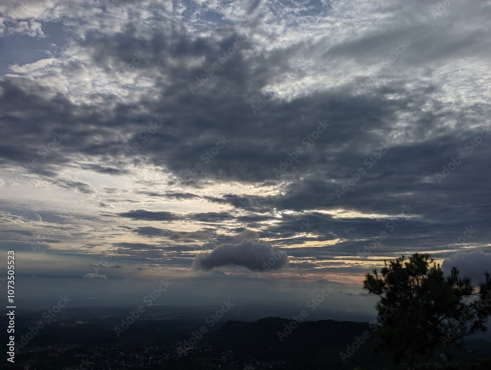 Dramatic sunset sky with layered clouds over a sprawling valley vista. A captivating view of a valley landscape at sunset, shrouded in a dramatic sky filled with layered grey and white clouds. Dramatic sunset sky with layered clouds over a sprawling valley vista. A captivating view of a valley landscape at sunset, shrouded in a dramatic sky filled with layered grey and white clouds.