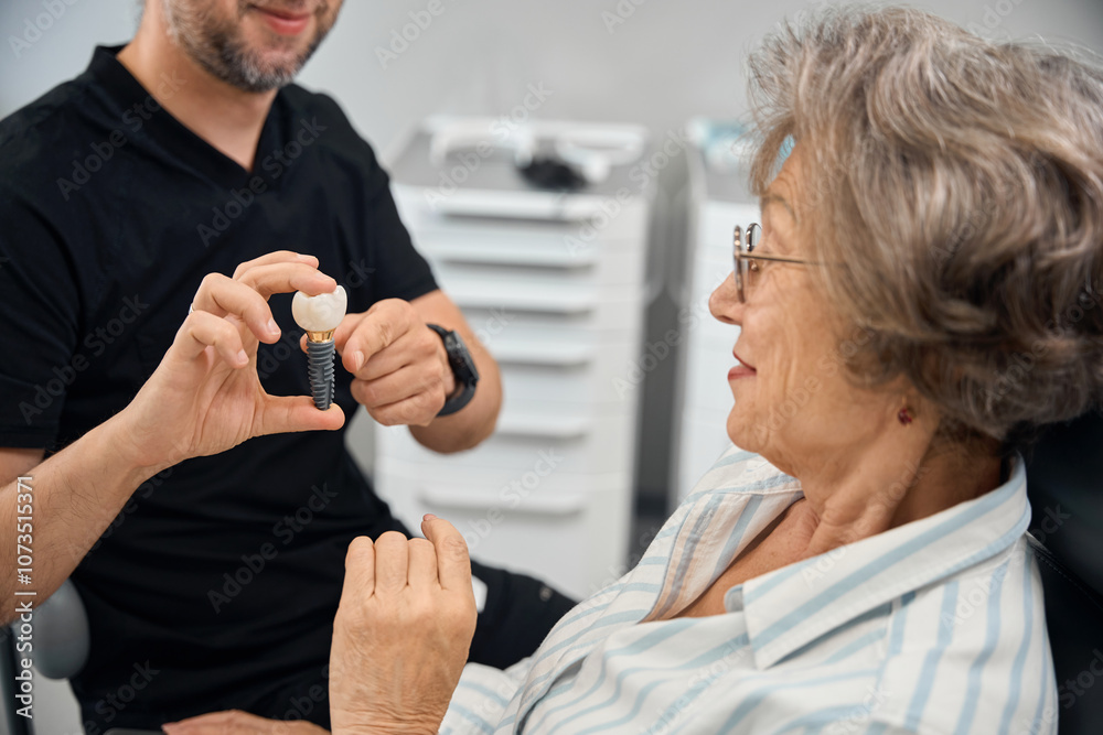 Patient examines model of dental implant in hands of dental prosthetist