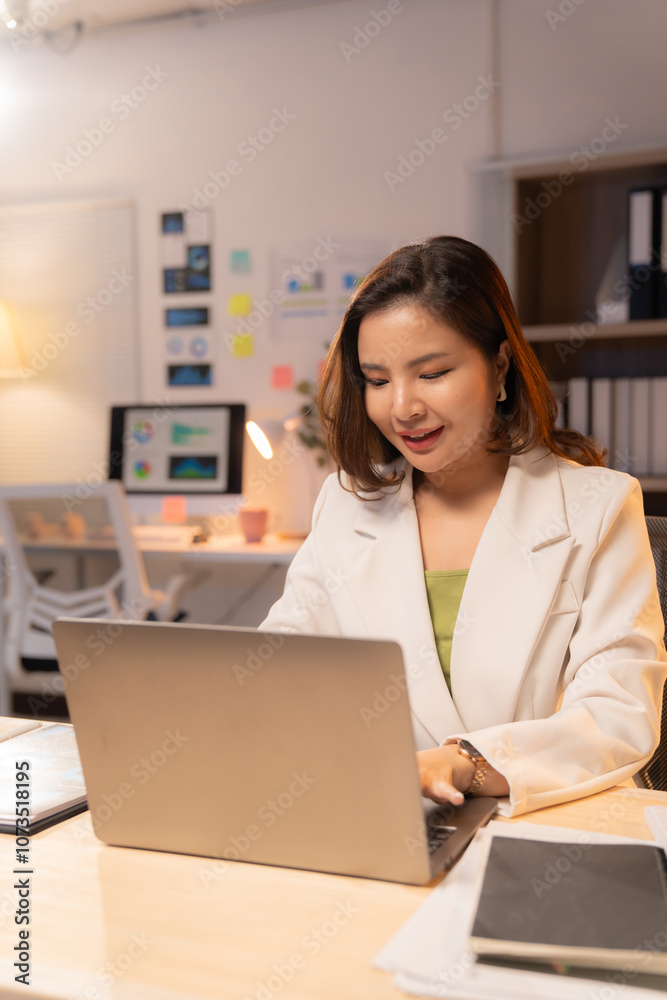 Young asian businesswoman smiling and working on a laptop in a modern office at night, focused on her tasks and enjoying the quiet atmosphere Young asian businesswoman smiling and working on a laptop in a modern office at night, focused on her tasks and enjoying the quiet atmosphere