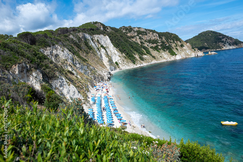 Sansone beach at the Elba island in summer, with sunbeds and sun umbrella with many bathers at the seashore and yellow pedalo at anchor