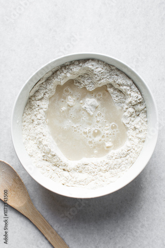 Overhead view of artisan bread dough being mixed in a white mixing bowl, top view of dry bread dough, process of making white bread