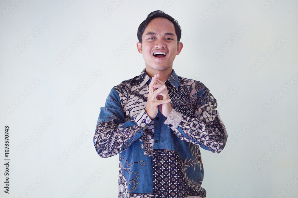 Smiling Asian man wearing batik shirt, showing hand gesture of apology and welcome. Advertising concept. Smiling Asian man wearing batik shirt, showing hand gesture of apology and welcome. Advertising concept.