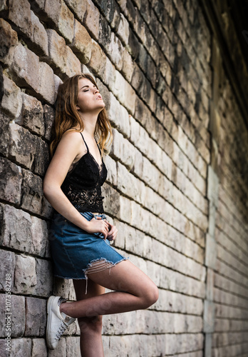 Beautiful 20 yo woman standing against a rough brick stone wall, Brussels, Belgium