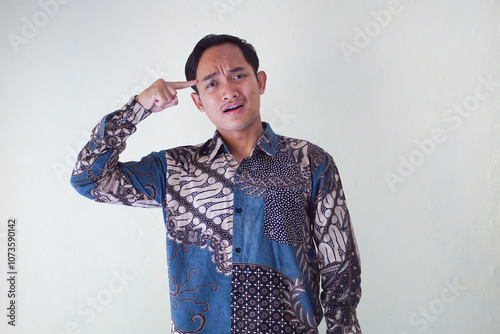 Handsome Asian young man wearing batik shirt showing gesture of thinking about something, memorizing on white background photo