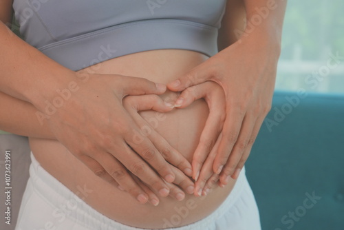 Obraz na płótnie Asian husband and wife stand hugging each other, father holding hands with wife making a heart shape on the womb, wife is 7 months pregnant and happy with first child. w salonie