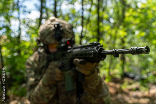 A soldier in full camouflage gear takes aim with a rifle in a wooded area, showcasing military equipment and focus in a natural setting. military operations in the forest