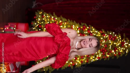 Blonde woman in red dress posing in front of Christmas tree. High quality photo