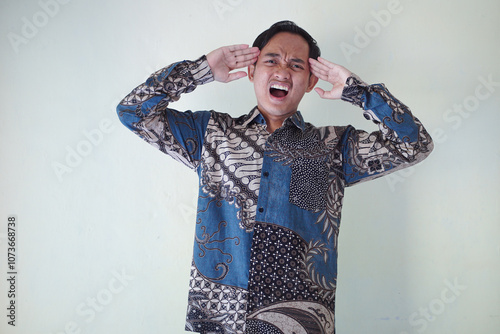 young Asian man wearing a batik shirt with a facial expression of surprise, surprise and amazement