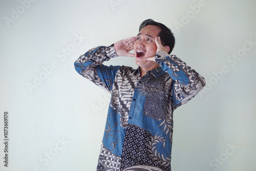 young Asian man wearing a batik shirt with a facial expression of surprise, surprise and amazement