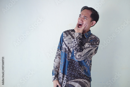 young Asian man wearing a batik shirt with a facial expression of surprise, surprise and amazement