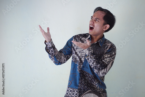 Excited young Asian man 20s wearing batik shirt pointing finger up, having great idea isolated on white background