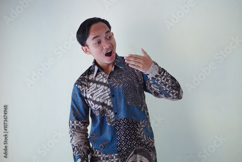 young Asian man wearing a batik shirt with a facial expression of surprise, surprise and amazement