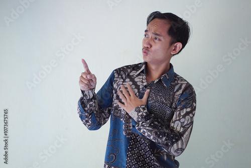 Excited young Asian man 20s wearing batik shirt pointing finger up, having great idea isolated on white background