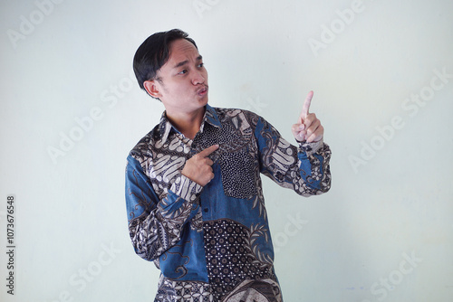 Excited young Asian man 20s wearing batik shirt pointing finger up, having great idea isolated on white background
