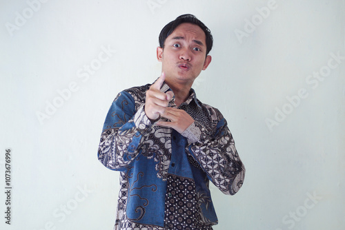 Excited young Asian man 20s wearing batik shirt pointing finger up, having great idea isolated on white background