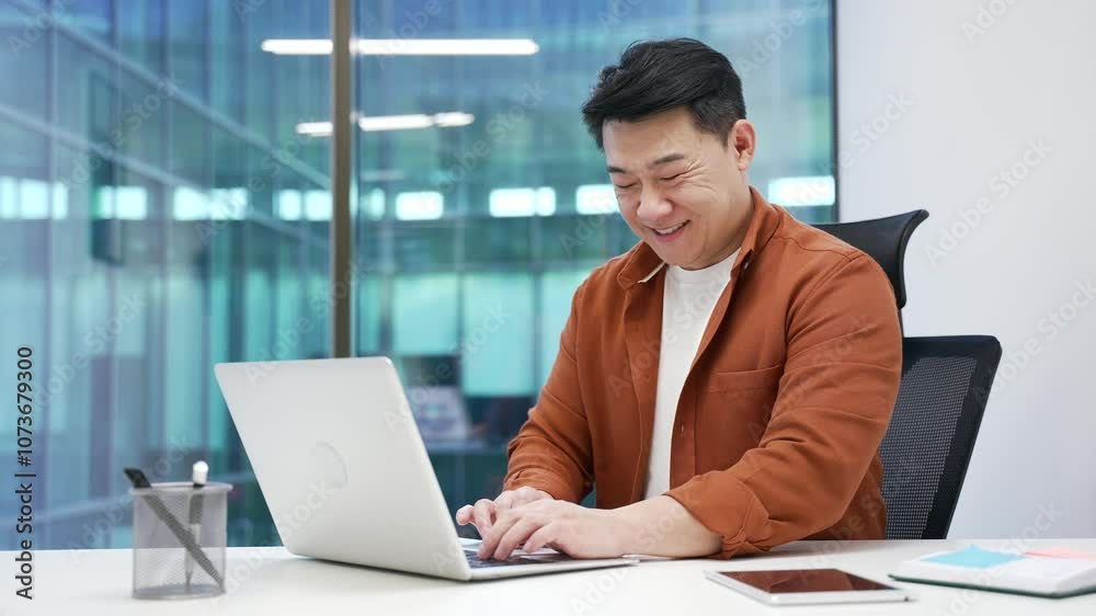 Confident Asian businessman typing on laptop sitting at workplace in business office. Smiling male worker working in computer application, banking, texting a client, chatting online. busy with project Confident Asian businessman typing on laptop sitting at workplace in business office. Smiling male worker working in computer application, banking, texting a client, chatting online. busy with project