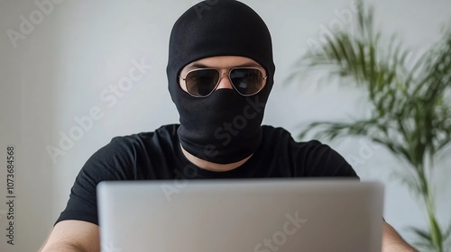 A hacker wearing a balaclava and a black t-shirt, sitting in front of a laptop. The atmosphere is tense and mysterious, with a sense of secrecy as the hacker focused intently on the screen.