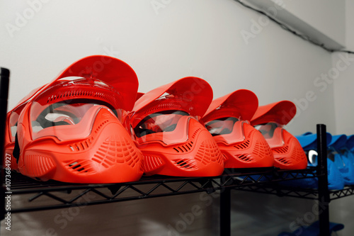 A row of red protective paintball masks on a black shelf. photo