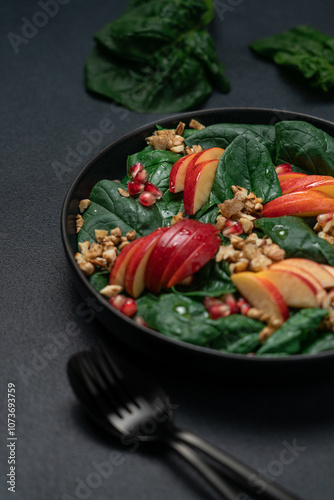 Fototapeta Naklejka Na Ścianę i Meble -  Seasonal salad with pomegranate seeds, walnuts, apples and spinach in a black plate on a dark background, side view