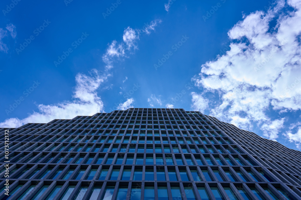 Looking up at a tall, modern skyscraper with glass windows reflecting a clear blue sky. The buildings design is sleek and urban, showcasing contemporary architecture against an open, cloudless Looking up at a tall, modern skyscraper with glass windows reflecting a clear blue sky. The buildings design is sleek and urban, showcasing contemporary architecture against an open, cloudless