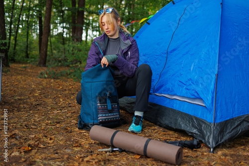 Female hiker packing backpack near tent in forest