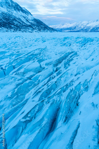 Flying over the frozen landscape of the Knik river, between snowcapped mountains through the icy winter wonderland of Knik Glacier with its icy blue glacial patterns photo