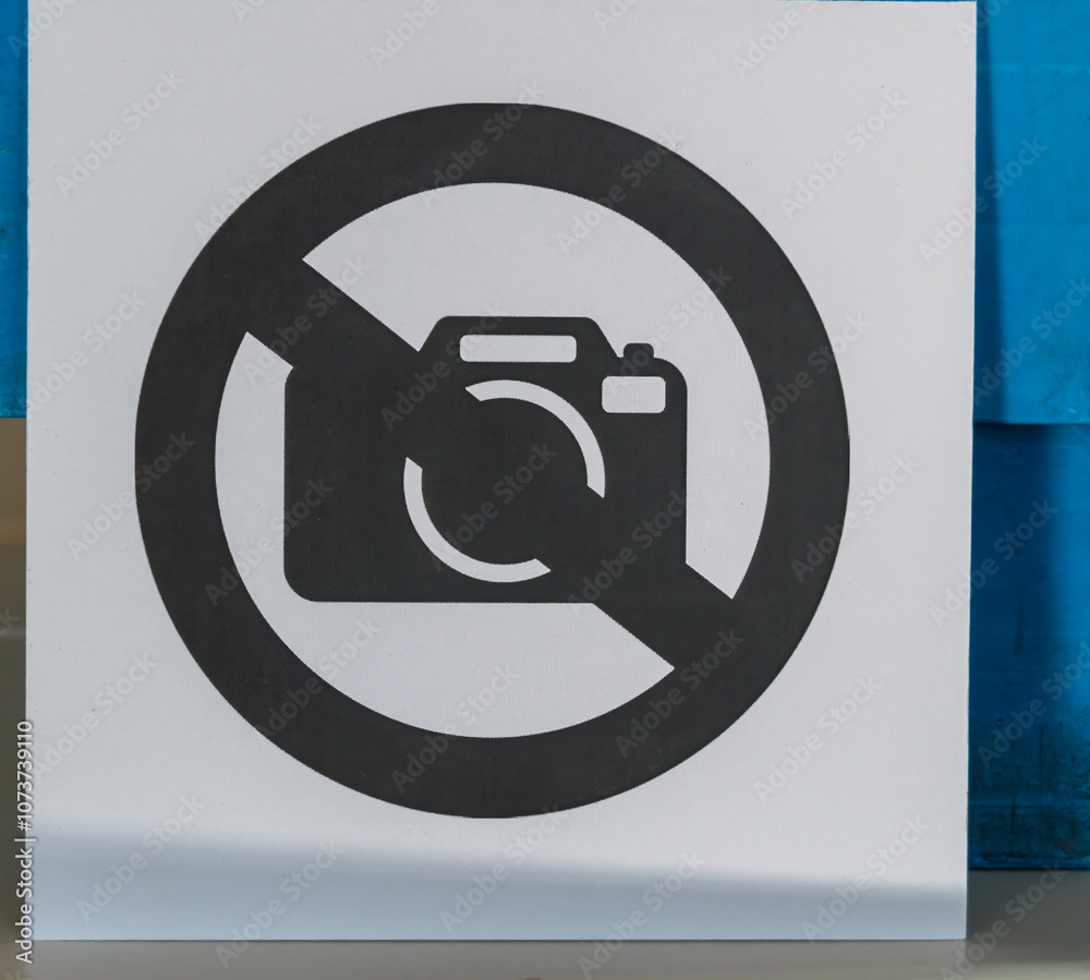 A clear sign is displayed, indicating that photography is not allowed in this area. The background features a blue wall, complementing the straightforward messaging A clear sign is displayed, indicating that photography is not allowed in this area. The background features a blue wall, complementing the straightforward messaging