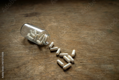 A few tablets of alpha lipoic acid spilling out of the bottle.Active additives in capsules.The glass jar with the medicine is scattered on the table. photo