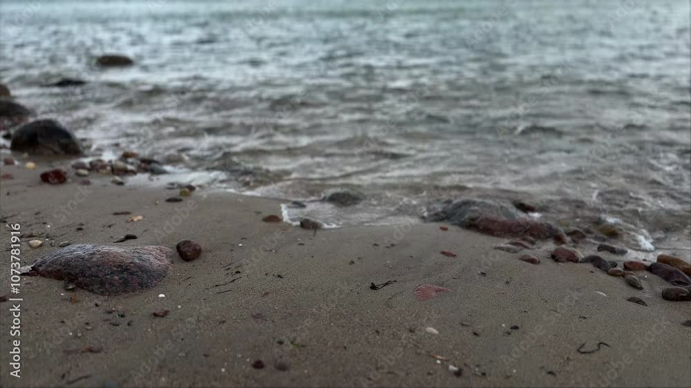 Waves on the beach. Stones on a sandy sea beach washed by water, windy weather by the sea. Sea beach in autumn. Waves on the beach. Stones on a sandy sea beach washed by water, windy weather by the sea. Sea beach in autumn.