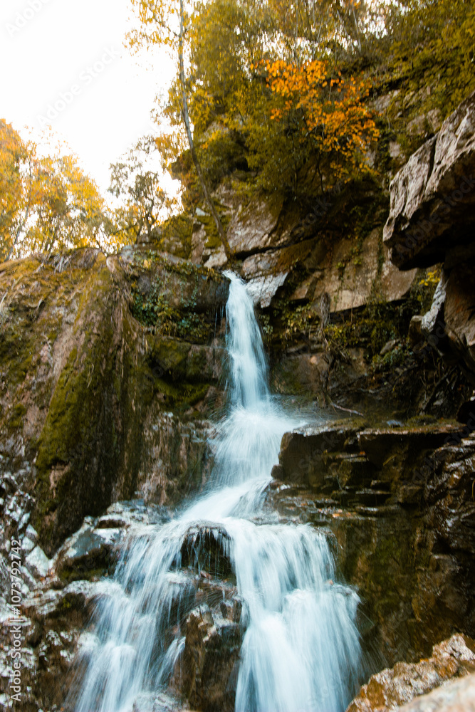 Serene waterfall cascades down moss-covered rocks, surrounded by the vibrant colors of autumn foliage. Serene waterfall cascades down moss-covered rocks, surrounded by the vibrant colors of autumn foliage.
