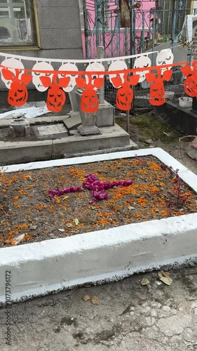 Halloween and Day of the Dead garlands hang over old grave decorated with flowers