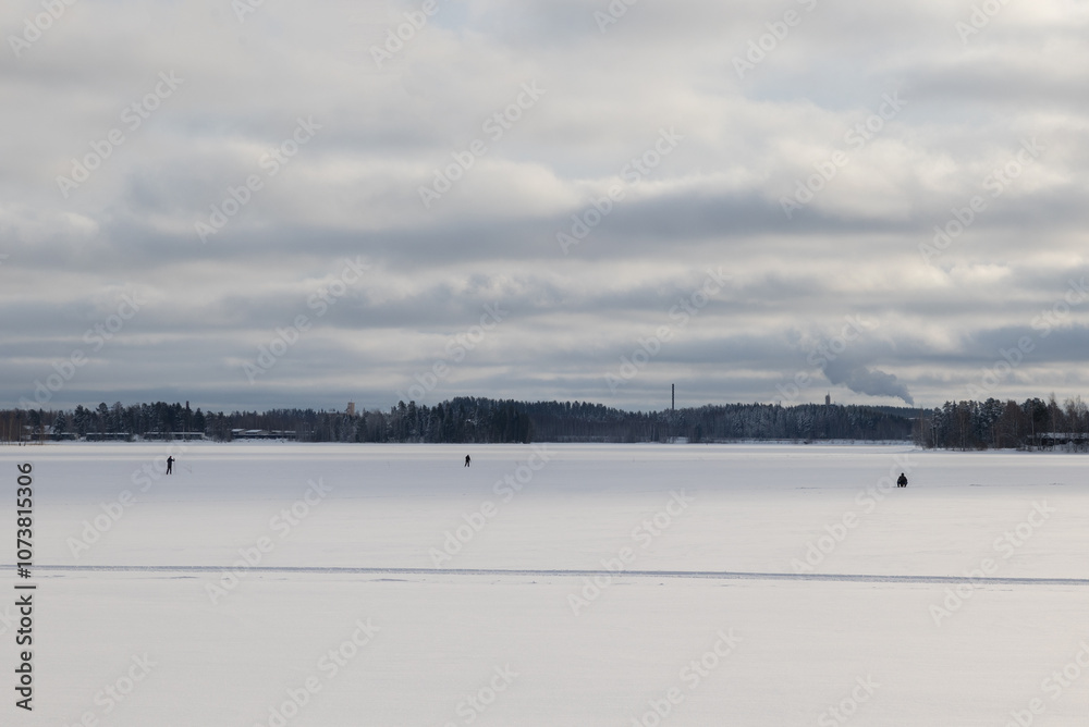 Frozen lake with ice fishermen in a tranquil winter landscape under cloudy skies Frozen lake with ice fishermen in a tranquil winter landscape under cloudy skies