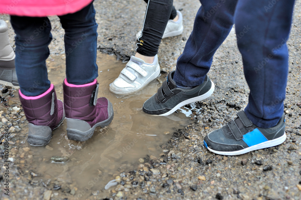 Horizontal photograph of 4 unrecognizable children sticking their feet in sports shirts and wellies in a small puddle of water. Selective focus. Copy space Horizontal photograph of 4 unrecognizable children sticking their feet in sports shirts and wellies in a small puddle of water. Selective focus. Copy space