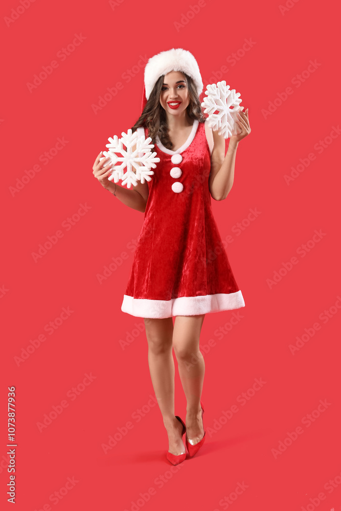 Young woman in Santa costume with snowflakes on red background. New Year celebration Young woman in Santa costume with snowflakes on red background. New Year celebration