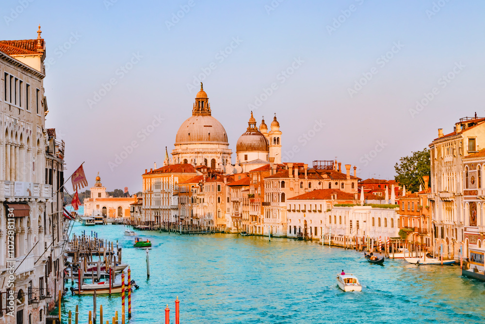 Beautiful view of traditional Gondola on famous Canal Grande with Basilica di Santa Maria della Salute in golden evening light at sunset in Venice, Italy.