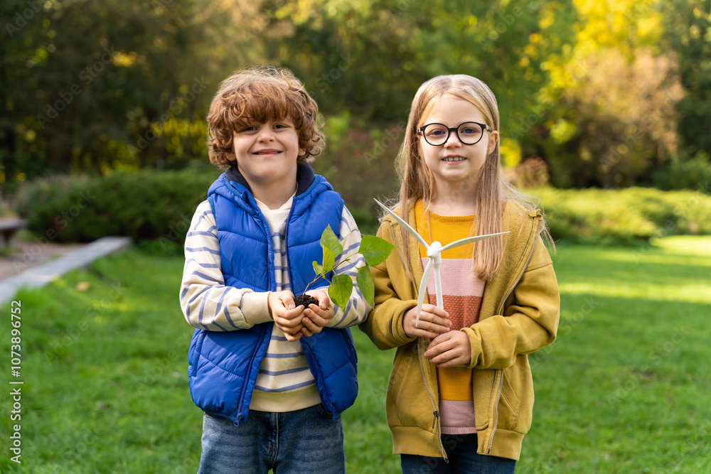 Obraz premium Children holding young plant and model of wind turbine symbolizing renewable energy growth