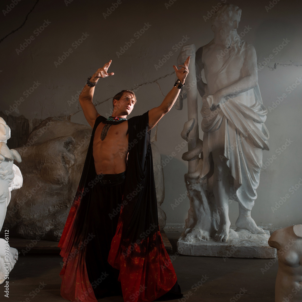 Fototapeta premium Muscular charismatic bodybuilder model in a silk cape makes an expressive pose, sculptor's workshop