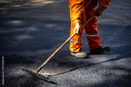 Worker finishing asphalt surface repair on a road during daytime at a construction site in an urban area