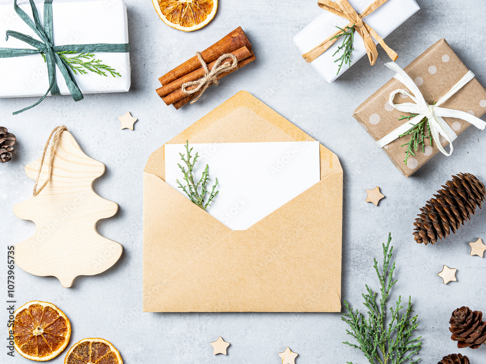 Envelope with a blank card decorated with a small sprig of greenery, surrounded by gift boxes wrapped with twine, pine cones, dried orange slices, and wooden ornaments on a light background. Envelope with a blank card decorated with a small sprig of greenery, surrounded by gift boxes wrapped with twine, pine cones, dried orange slices, and wooden ornaments on a light background.