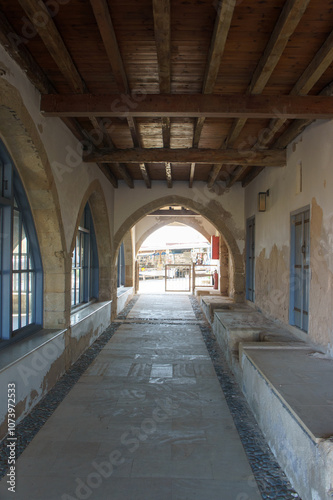 A tranquil corridor leads to a sunlit courtyard in a historic building during the afternoon.