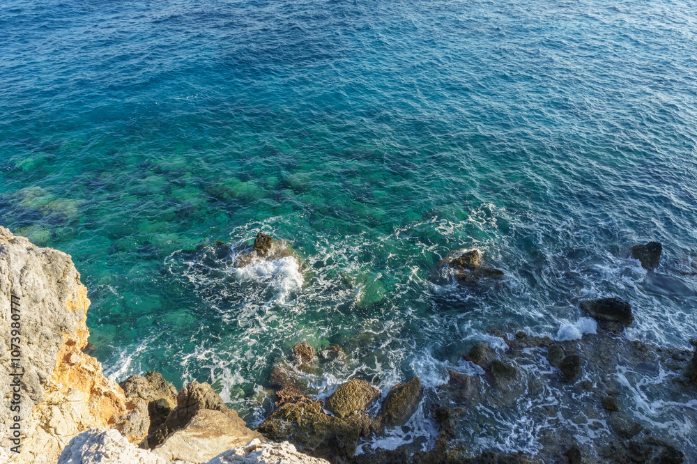 Calm ocean waves gently lap against rocky shores beneath a clear blue sky at midday. Calm ocean waves gently lap against rocky shores beneath a clear blue sky at midday.